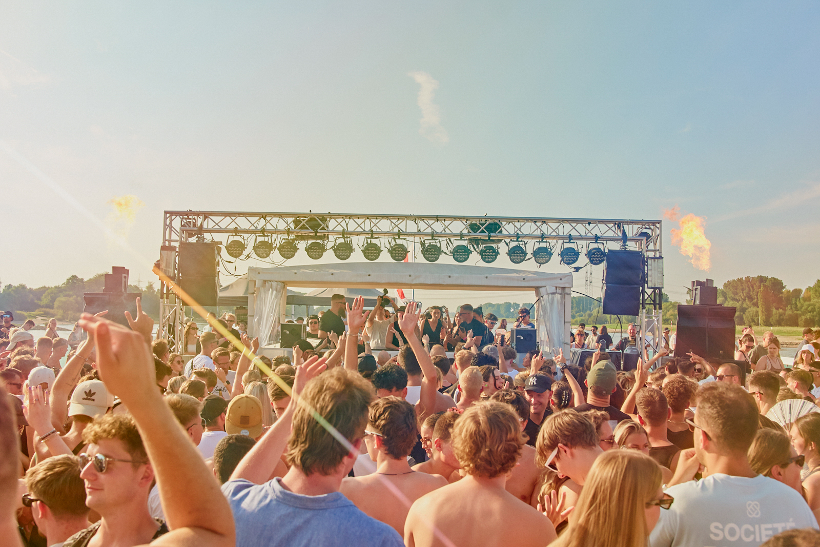 Feiernde Menschen von hinten auf einem Schiff, die Richtung DJ Pult gucken und ihre Hände zur Musik in die Luft strecken