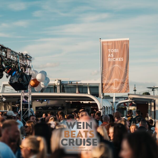 Feiernde Menschen auf einem Schiff vor dem Banner vom Weingut Tobias Rickes