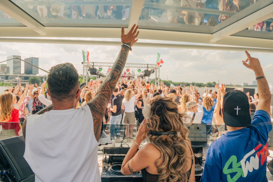 Zwei DJS und eine Djane an den Turntables sprechen zur feierenden Menge