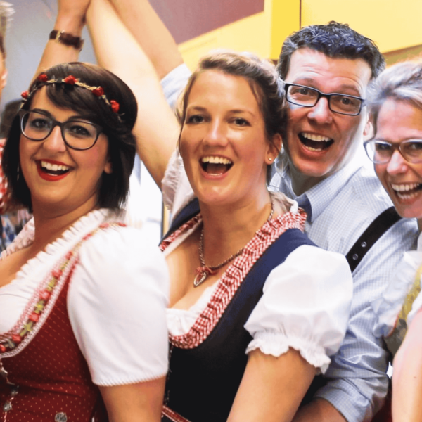 Six cheerfully celebrating people in Oktoberfest clothing look into the camera