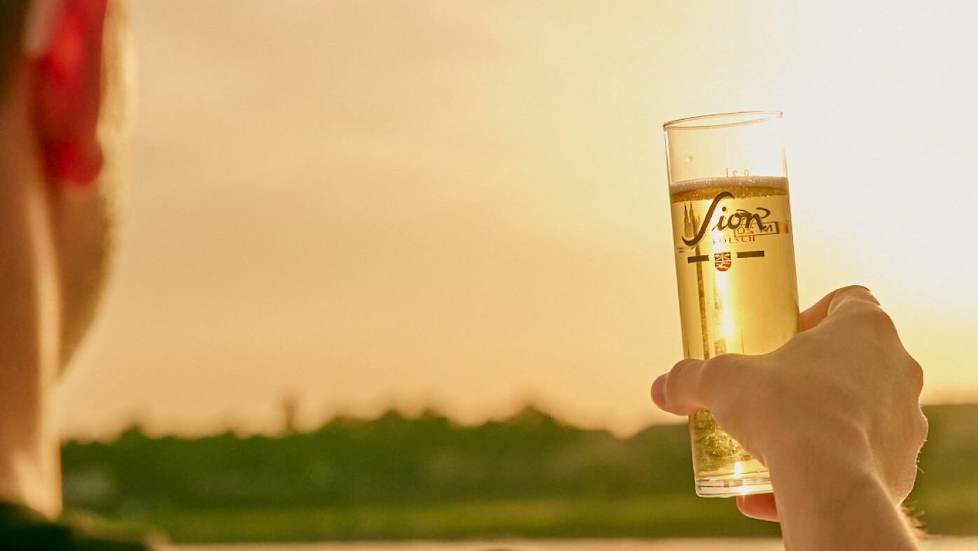 Mann hält gefülltes Sion Kölsch Glas in die untergehende Sonne