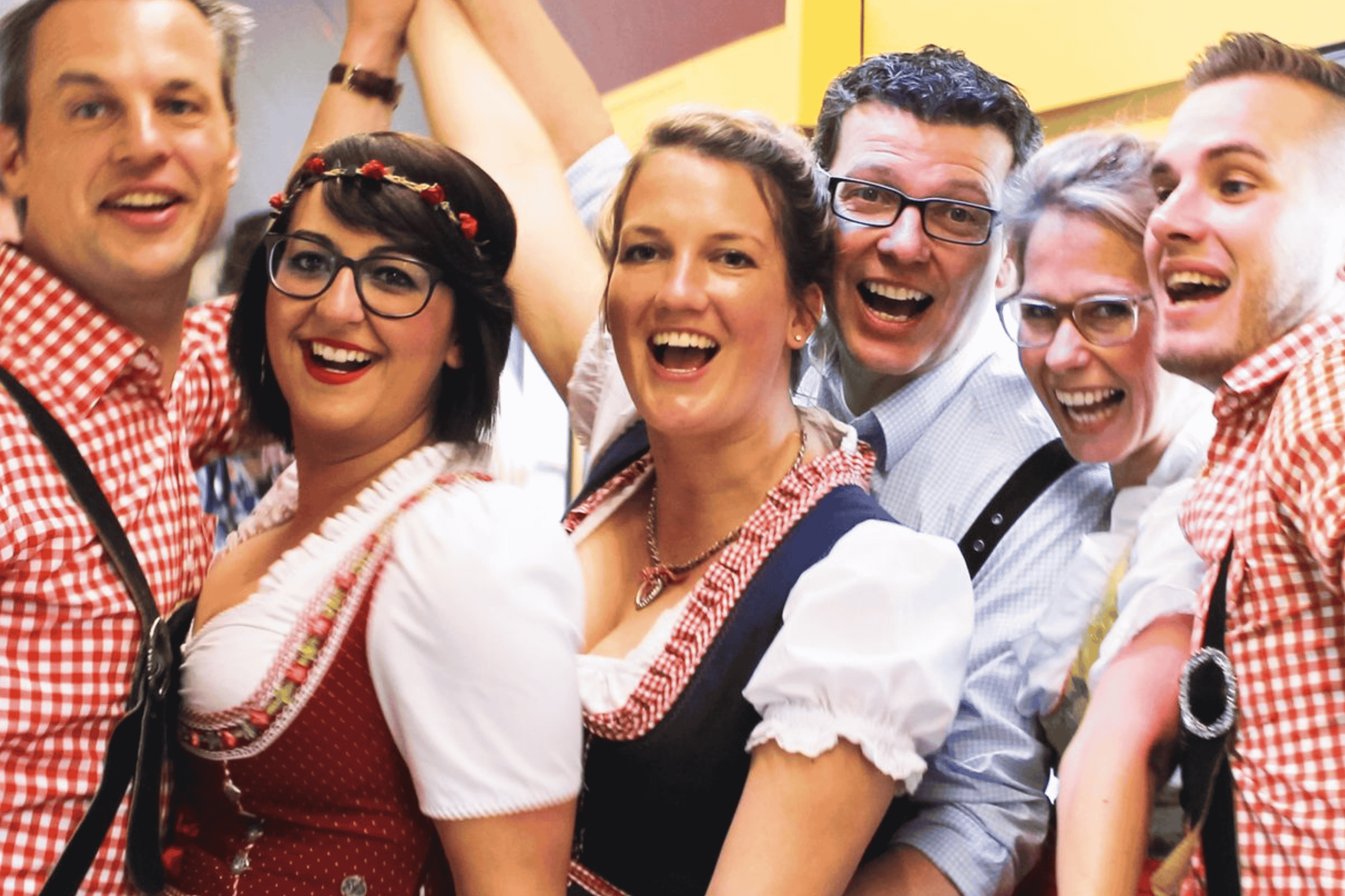 Six cheerfully celebrating people in Oktoberfest clothing look into the camera